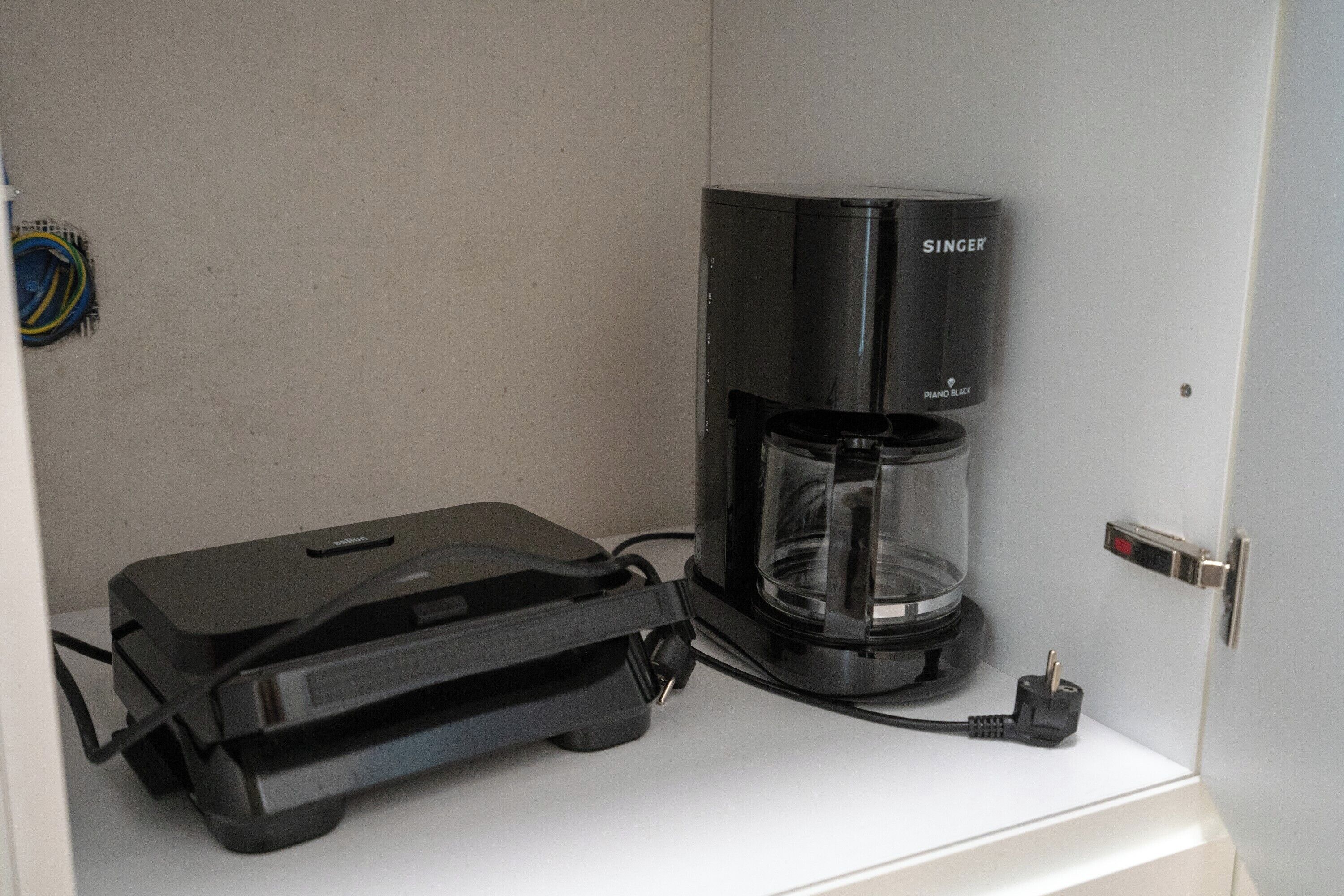 A coffee maker and a portable electronic device on a white surface.