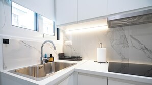 Ett modernt kök med en diskho i rostfritt stål, vita skåp och en inbyggd spis.