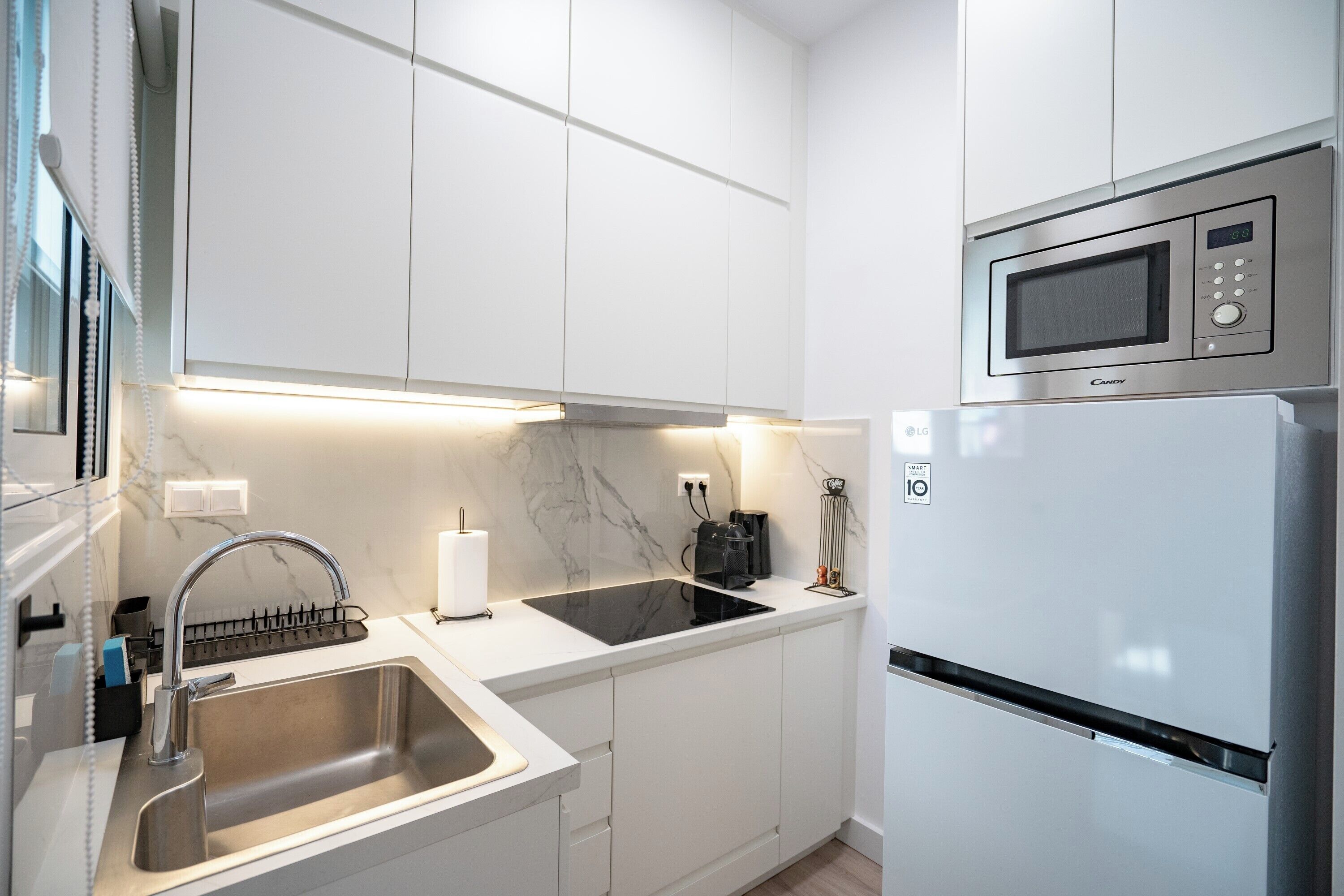 A modern kitchen with white cabinets, a stainless steel sink, a built-in microwave, and a refrigerator.