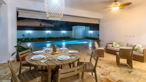 A dining area with a round table set for six, surrounded by wicker chairs. A pool is visible in the background, and there is a ceiling fan above the table. - Villa Valentina Oceanfront Bliss (Sosúa)