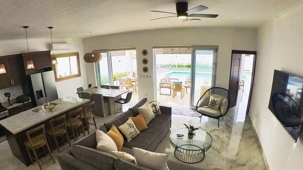 A modern living space with a kitchen, dining area, and a balcony with a pool view. - Villa Valentina Oceanfront Bliss (Sosúa)