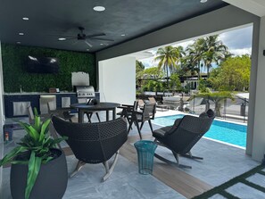 Une terrasse extérieure avec une piscine, des sièges, un barbecue et une vue sur l’eau.
