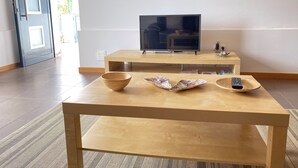 Ein modernes Wohnzimmer mit einem Holztisch, einem Fernseher auf einem Schrank und dekorativen Gegenständen auf Regalen.