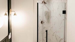 Un baño con lavamanos de mármol, ducha con mampara de vidrio y espejo instalado en la pared.