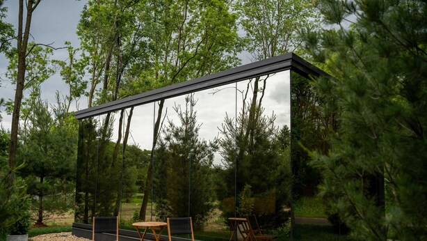 Un espacio moderno para sentarse al aire libre con cerramiento de vidrio, rodeado de árboles y un camino de grava.