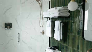 Un baño moderno con ducha de vidrio, inodoro blanco, lavamanos con encimera de mármol y tocador negro con tiradores dorados.