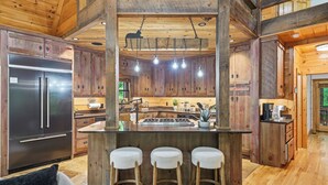 A wooden cabin-style kitchen with a central island, bar stools, and a stainless steel refrigerator.