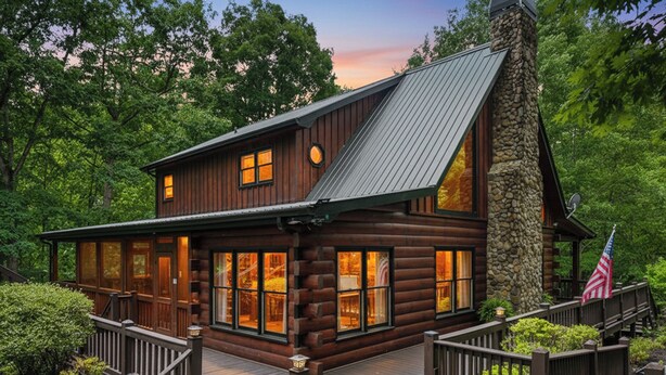 A log cabin with a stone chimney, a deck, and an American flag.