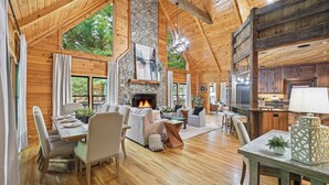 A spacious living room with a fireplace, wooden ceiling, and large windows.