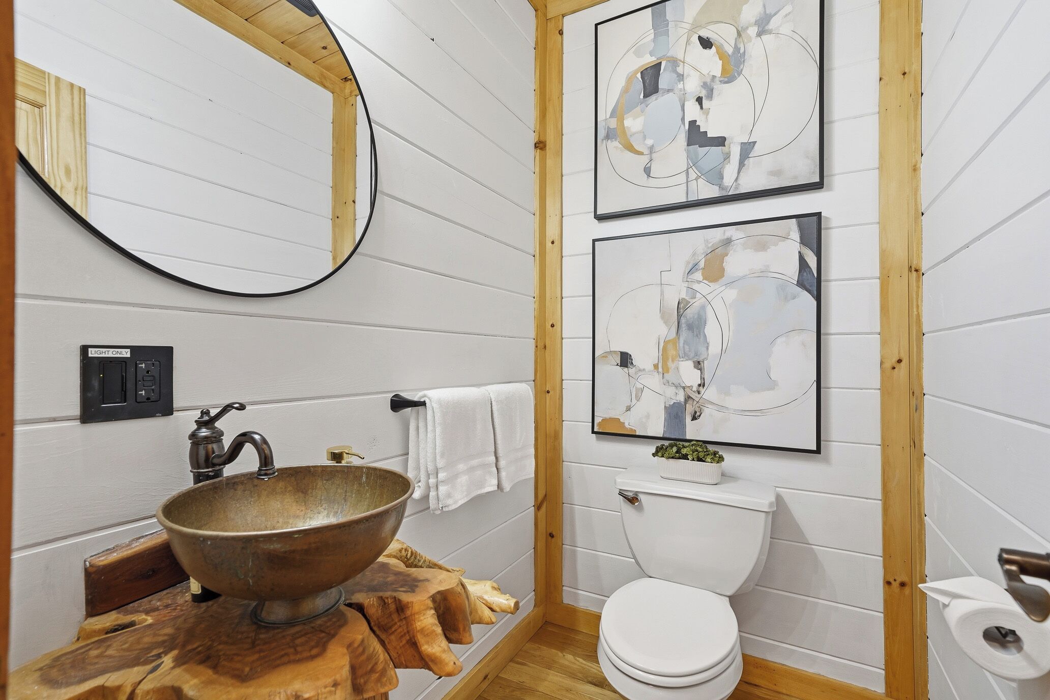 Een badkamer met een houten wastafel, toilet en abstracte kunst aan de wand.