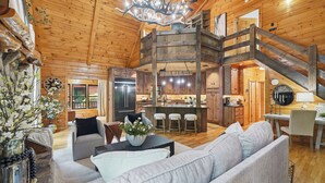A spacious log cabin interior with a central island kitchen, a dining area, and a living room with a large sofa.