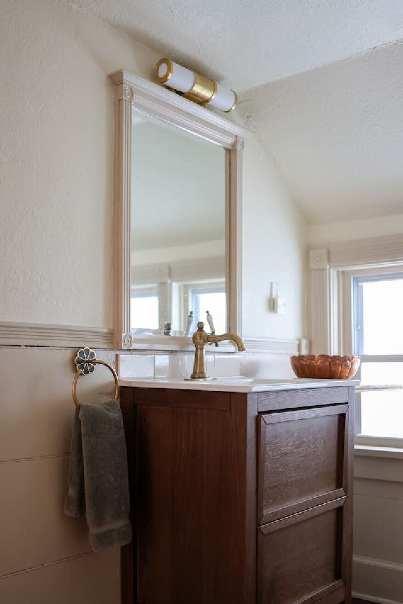 Un baño con tocador de madera, un espejo, un perchero para toallas y una ventana.