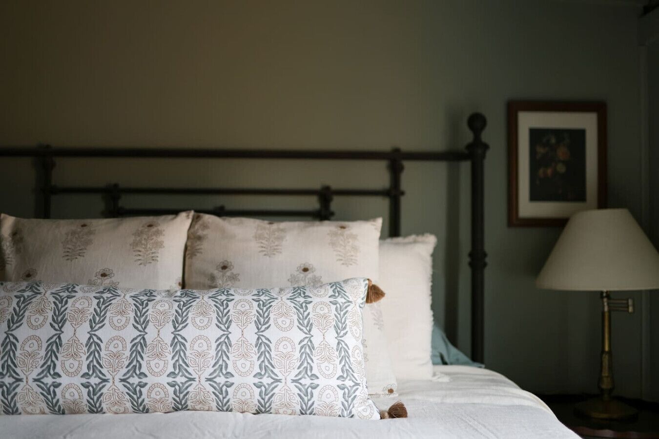 Un lit avec des coussins à motifs, une lampe de chevet et un tableau encadré au mur.