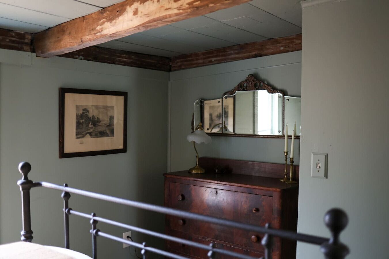 A bedroom with a wooden bed frame, a dresser, a mirror, and a framed picture on the wall.