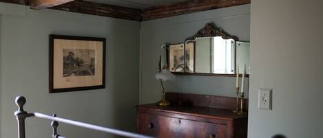 A bedroom with a wooden bed frame, a dresser, a mirror, and a framed picture on the wall.