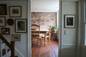 A hallway with a wooden staircase, a dining area with a brick wall, and framed pictures on the walls.