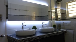 A modern bathroom with two sinks, a large mirror, and a small potted plant. - Friendly Beach House (Sandy Ground)