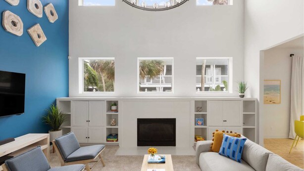 A living room with a fireplace, built-in shelving, a TV, and a large window overlooking a balcony.