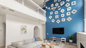 A living room with a high ceiling, a staircase, a flat-screen TV, and a blue accent wall. - Sleeps 18! Pool, Hottub, Game Room, Blocks to Beach Vilano Villa by Avantstay (St. Augustine)