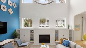 A living room with a TV, seating, a fireplace, and three windows with views of outdoor areas. - Sleeps 18! Pool, Hottub, Game Room, Blocks to Beach Vilano Villa by Avantstay (St. Augustine)