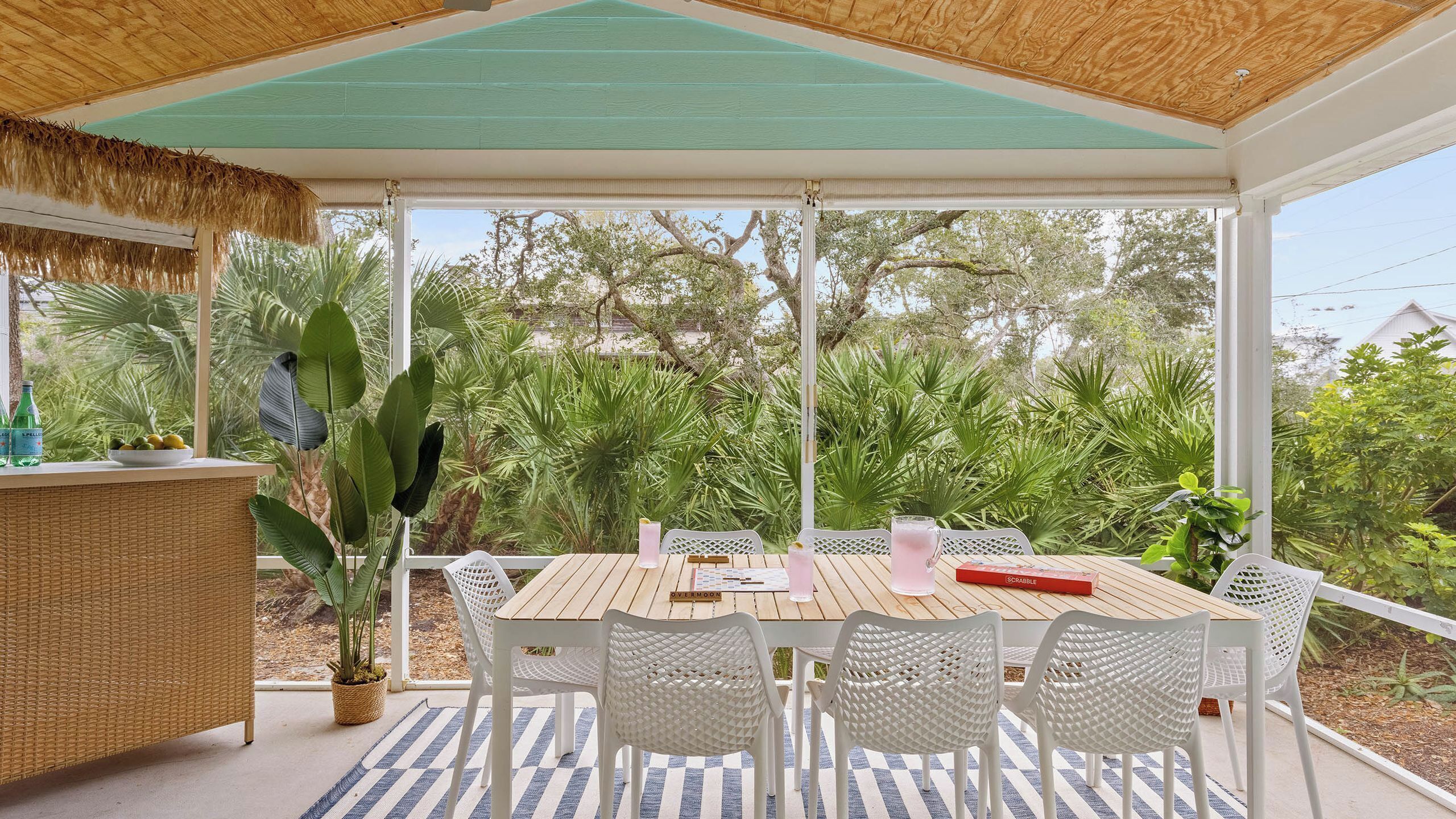 Un área de comedor al aire libre con mesa y sillas, rodeada de vegetación exuberante y un techo de paja.