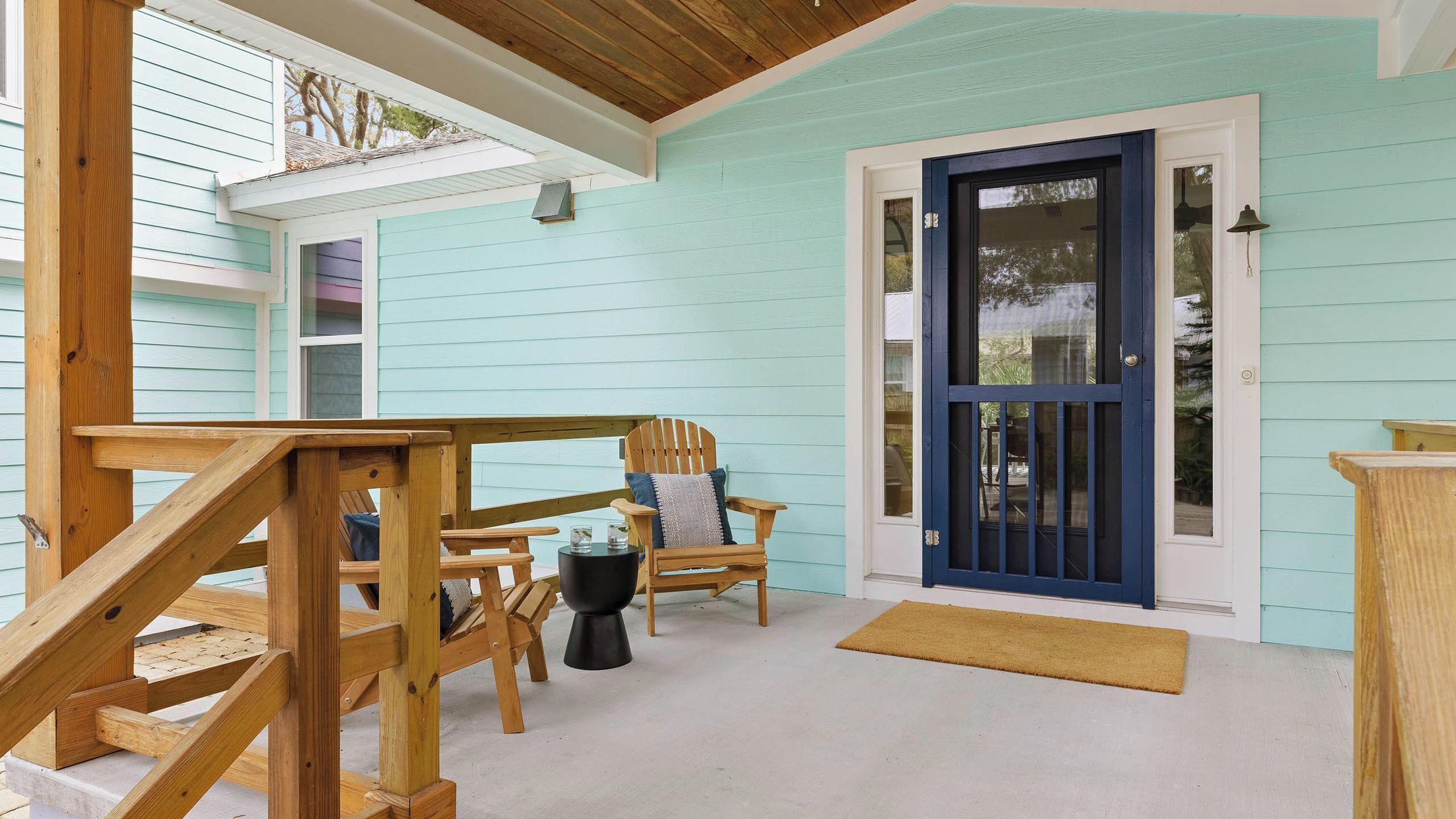 A wooden deck with a chair and a small table, a blue door, and a white exterior wall.