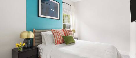 A bedroom with a bed, a nightstand, a ceiling fan, a window, and a framed picture on the wall.