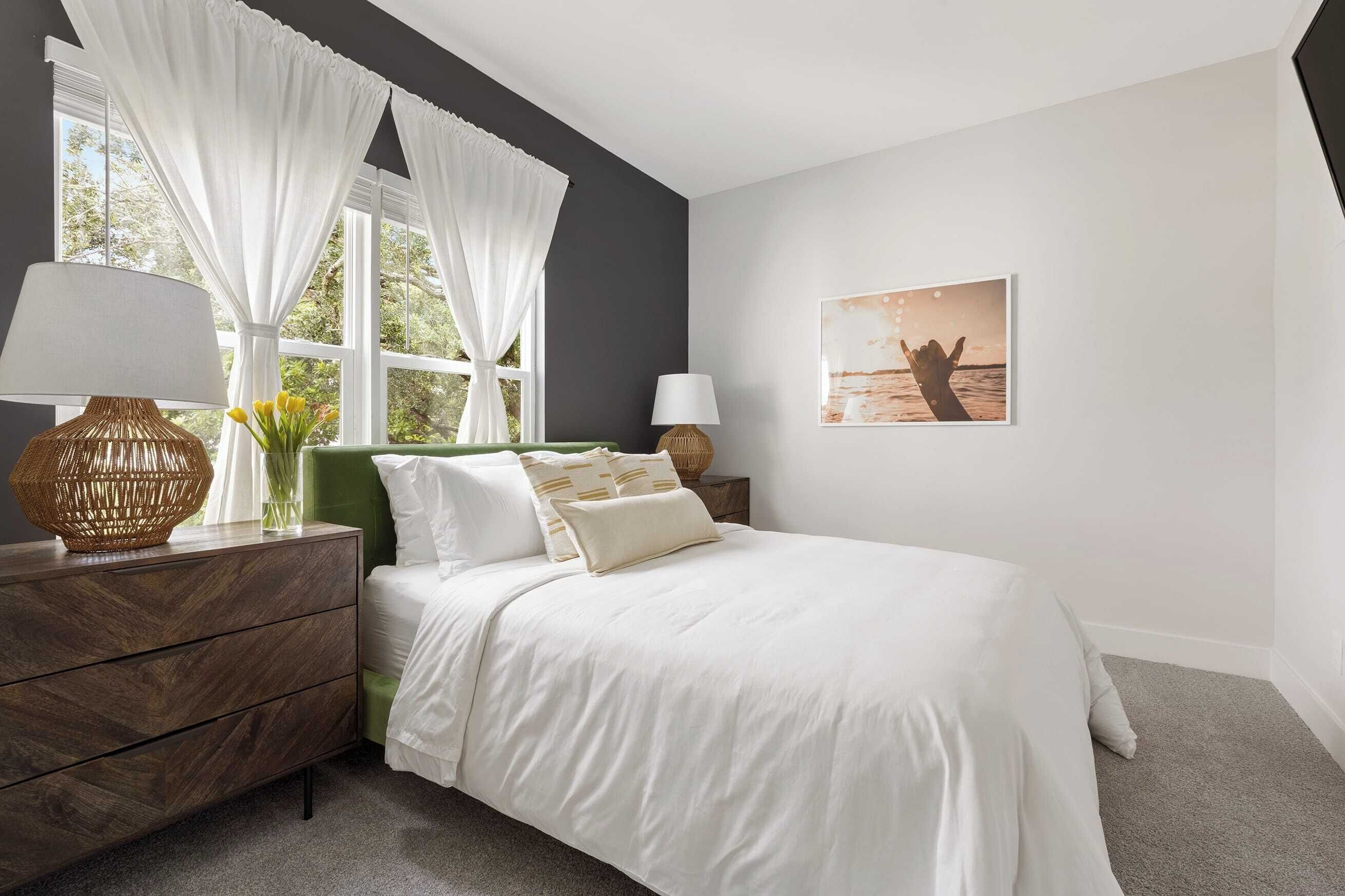 A bedroom with a bed, a dresser, a lamp, and a window with curtains.