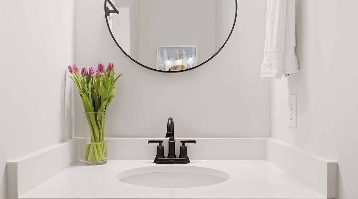 A bathroom with a white sink, a black faucet, a mirror, and a vase of pink tulips.
