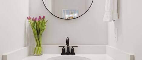 A bathroom with a white sink, a black faucet, a mirror, and a vase of pink tulips.