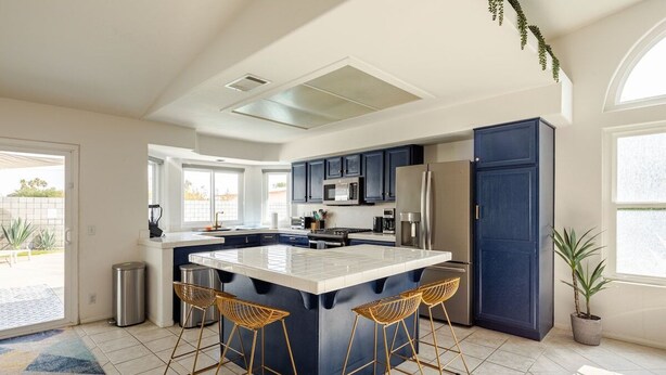 A modern kitchen with a central island, bar stools, and a large window. - Spacious, Bright 4-Bedroom Home with Mountain Views, Private Pool, and Hot Tub  (Palm Springs)