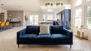 A modern living room with a dark blue sofa, a dining area with yellow chairs, and a kitchen with a dark blue refrigerator. - Spacious, Bright 4-Bedroom Home with Mountain Views, Private Pool, and Hot Tub  (Palm Springs)
