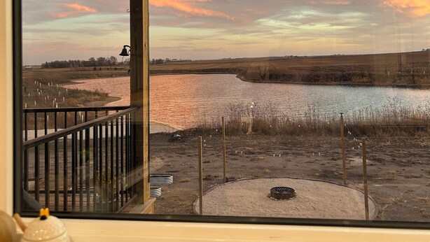 A view from a window overlooking a river and fields during sunset.