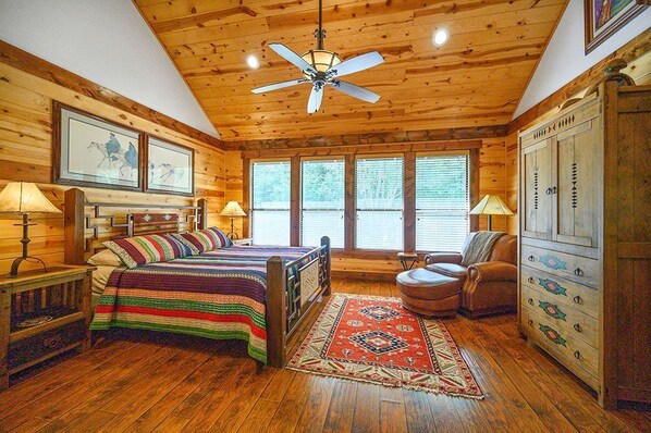 A log cabin bedroom with a bed, a chair, a dresser, and a ceiling fan.