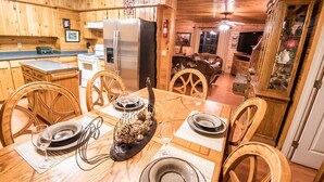 Interno di una baita in legno con un tavolo da pranzo per quattro persone, sedie in legno, un frigorifero, un fornello e una televisione nella zona soggiorno.