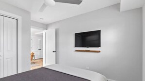 A bedroom with a bed, a ceiling fan, a mounted TV, and a door leading to another room. - Modern Renovated Suite in Riverside  (Riverside)