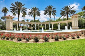 Une fontaine ornée de dauphins, entourée de palmiers et d’un jardin bien entretenu.