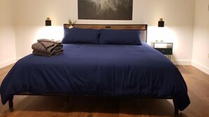 Un dormitorio con una cama grande, una mesita de noche, una lámpara de pared y un cuadro de un bosque.
