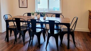 Un comedor con una mesa de madera y sillas negras, una araña y dos cuadros en la pared.