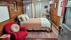 Une pièce de taille modeste, comprenant un lit, un fauteuil rouge, une petite table et un tapis.