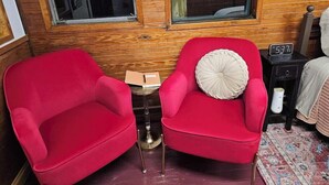Une pièce avec deux fauteuils rouges, une petite table sur laquelle se trouve un livre, une horloge et un mur en bois avec une inscription.