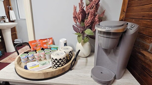 Une petite cuisine équipée d’une machine à café, d’un plateau de collations et d’un vase contenant des fleurs séchées.