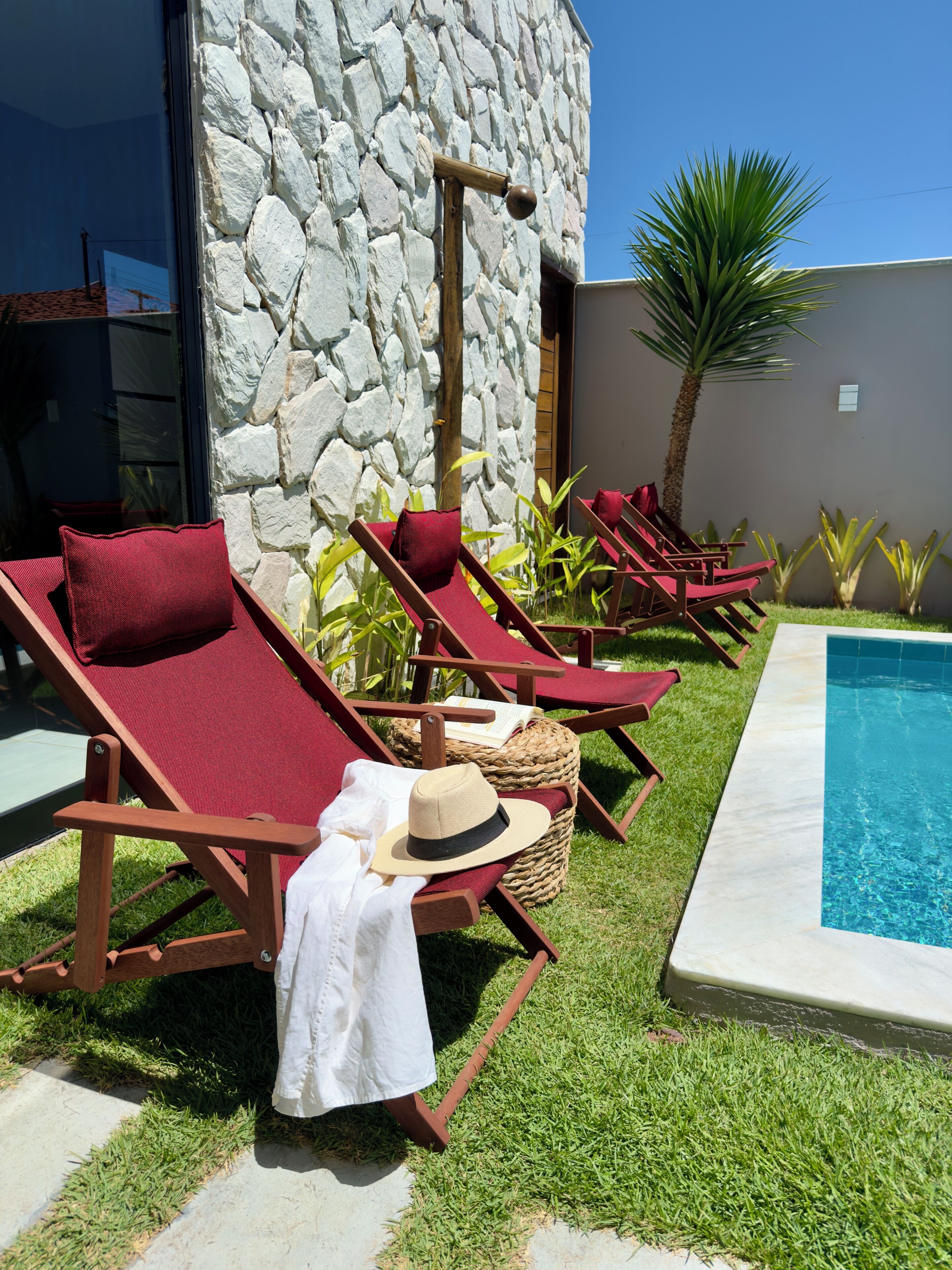 A poolside area with lounge chairs, a stone wall, and a clear blue sky.