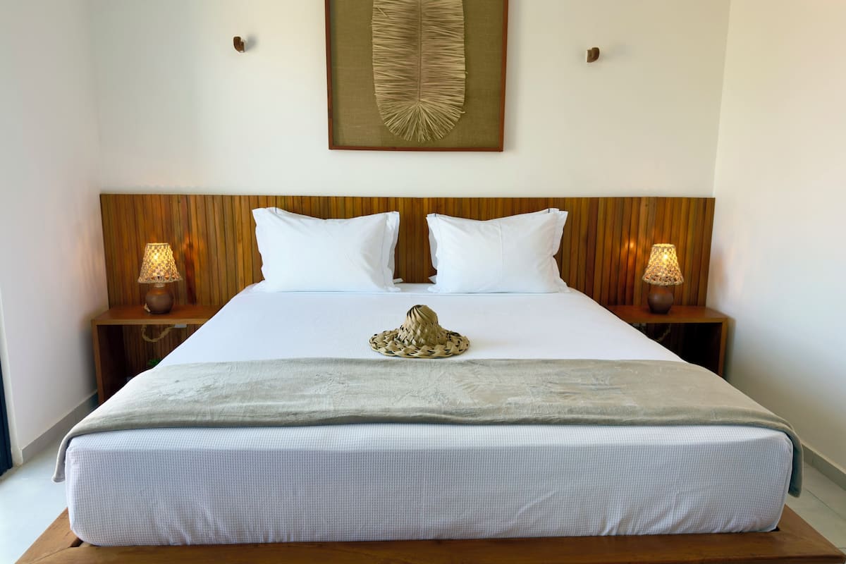 A neatly made bed with white linens, two bedside lamps, a framed artwork above the bed, and a wooden headboard.
