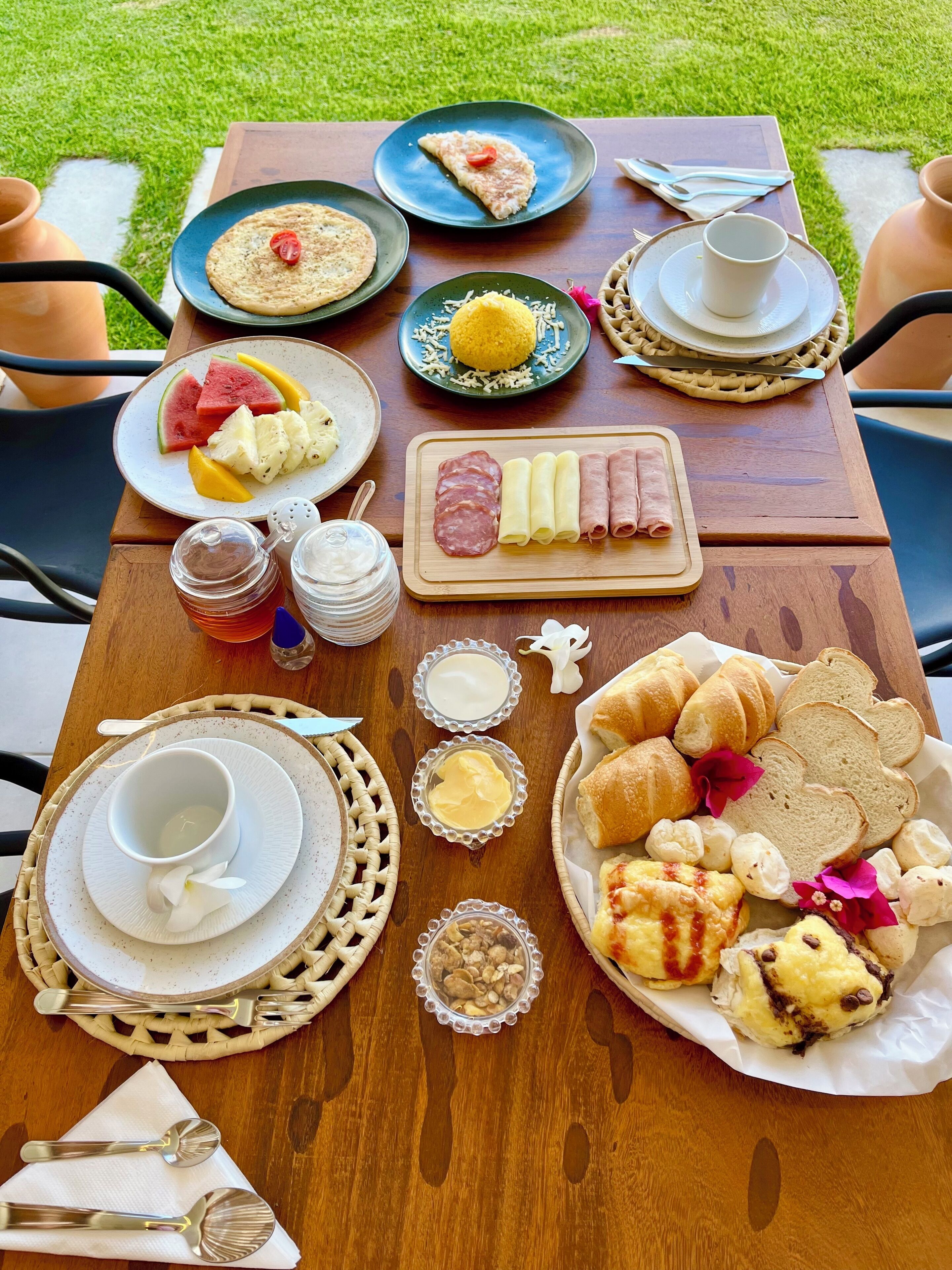 Una mesa dispuesta al aire libre con platos de comida, incluyendo frutas, pasteles y una tabla de quesos.