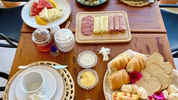 Una mesa dispuesta al aire libre con platos de comida, incluyendo frutas, pasteles y una tabla de quesos.