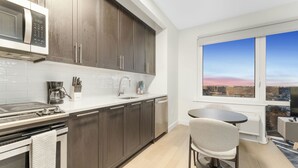 Une cuisine moderne avec des meubles en bois foncé, un plan de travail blanc et une vue sur la ville grâce à de grandes fenêtres.