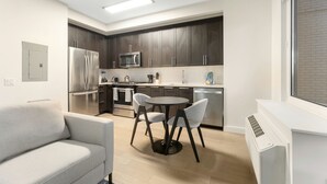 Une cuisine moderne avec des meubles de couleur sombre, des appareils en acier inoxydable et une table de salle à manger ronde, assortie de chaises.