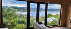 A room with a large window overlooking a lake, greenery, and distant hills. - xxxxxxxxxx (Chonchi)
