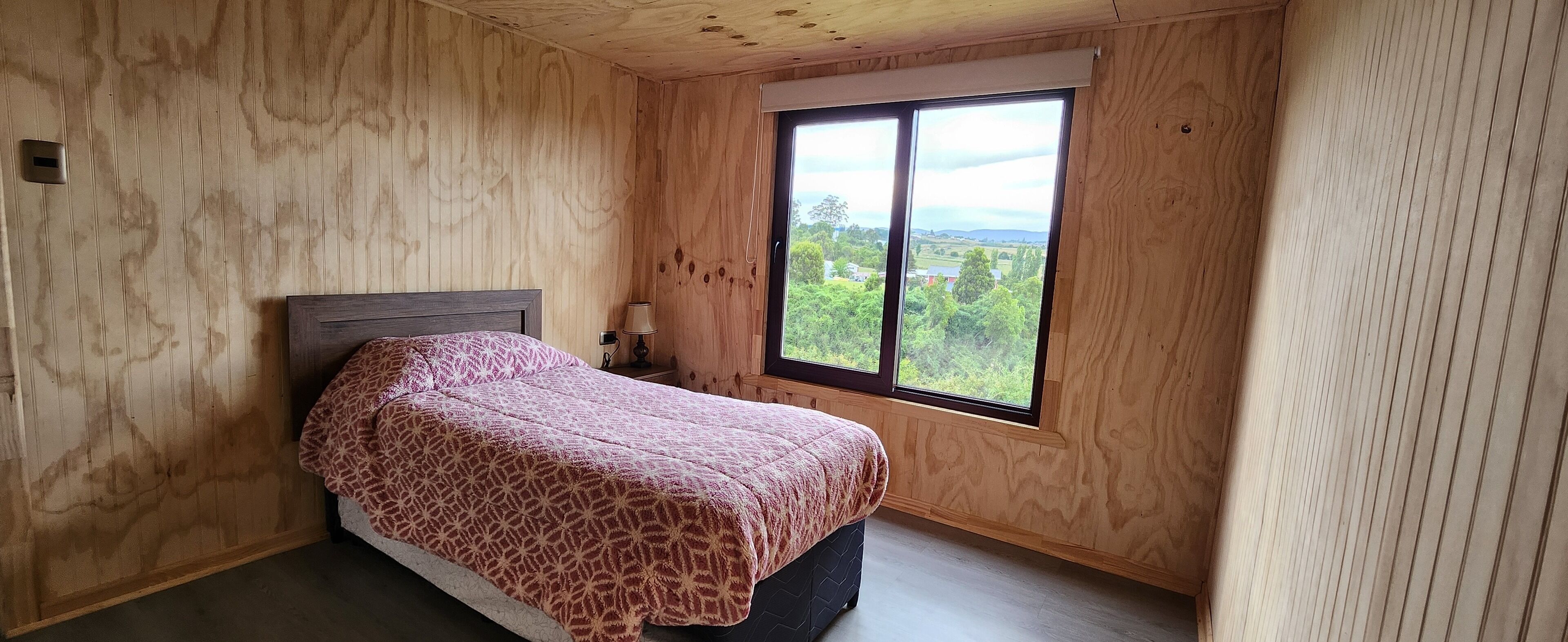Un dormitorio con una cama, una ventana y paredes de madera.